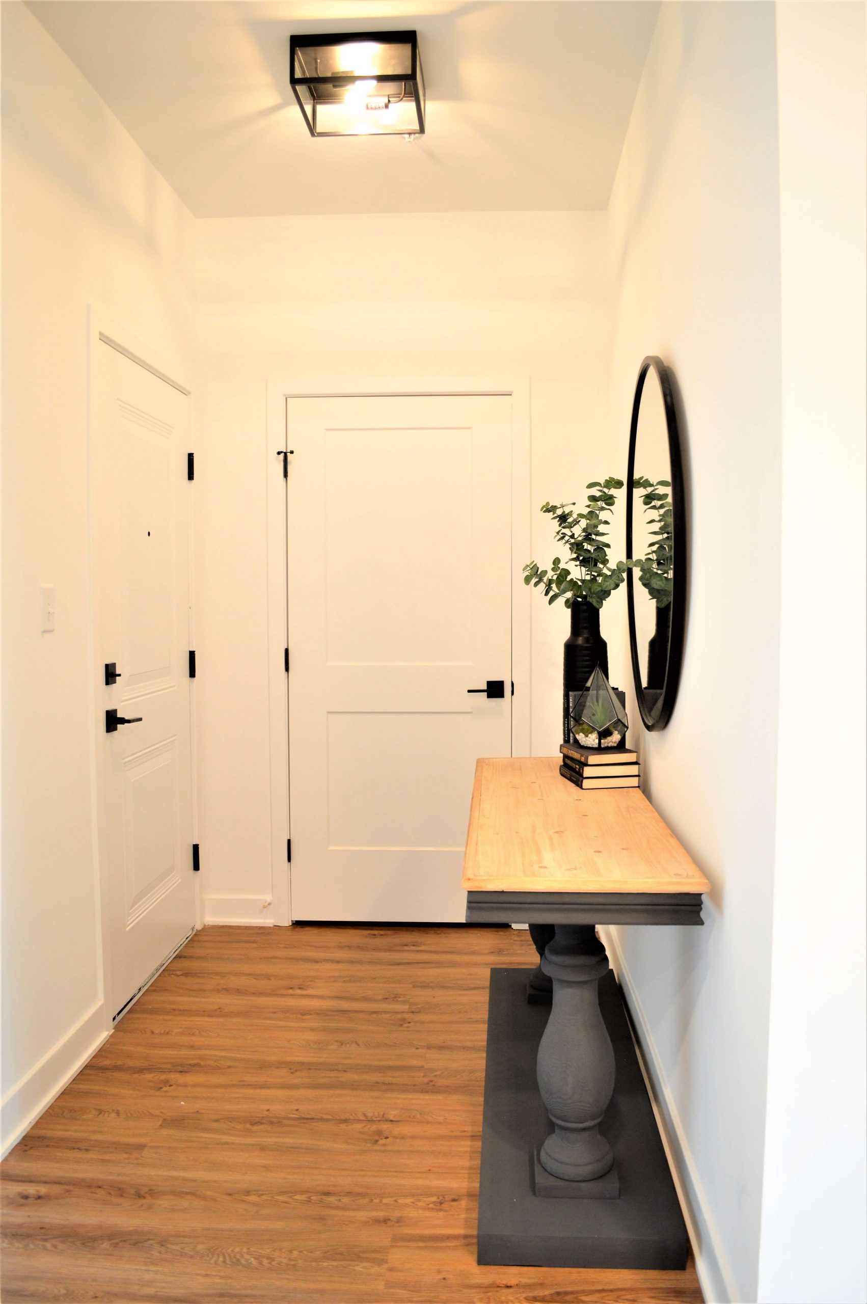 Entryway hallway with wood flooring, console table, round mirror, and white paneled doors