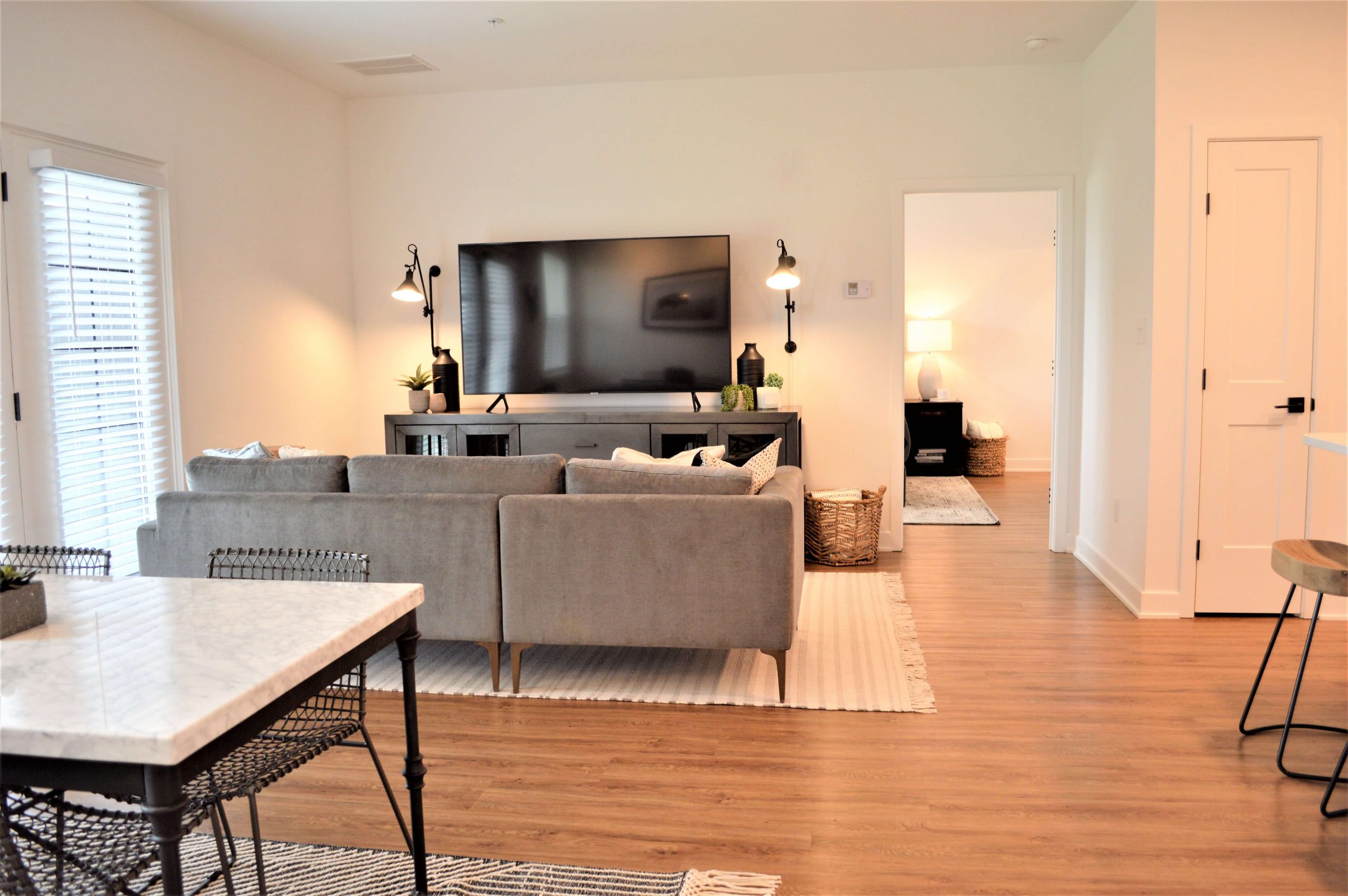 Open-concept living room with sectional sofa, mounted TV, wall sconces, and hallway leading to additional rooms