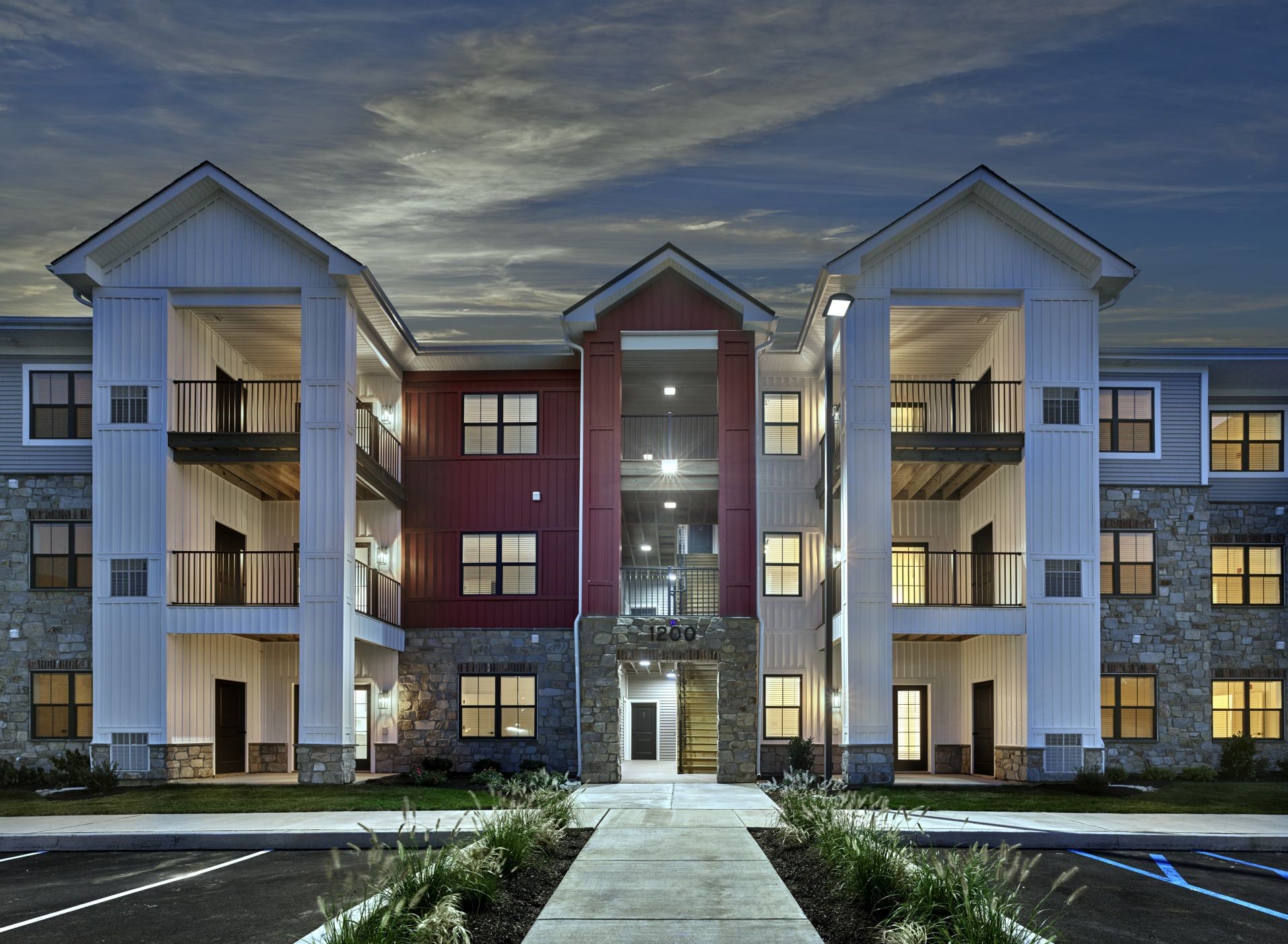Three-story apartment building entrance at dusk with stone accents, balconies, and illuminated walkway at The Reserve at Westown.