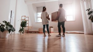 Adult man and woman carrying moving boxes in an empty room