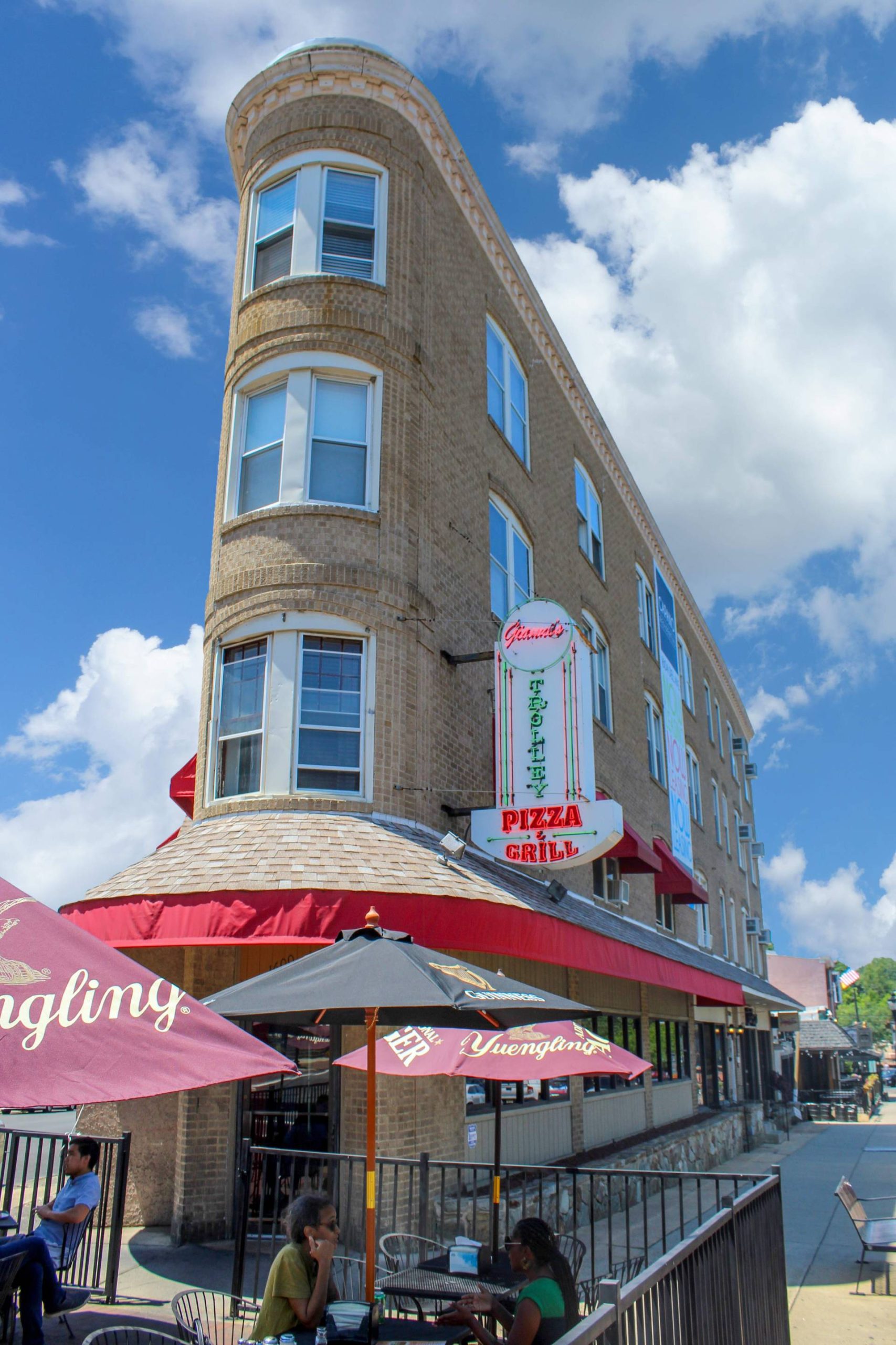 Corner building with rounded bay windows and outdoor cafe seating beneath a Trolley Pizza and Grill sign
