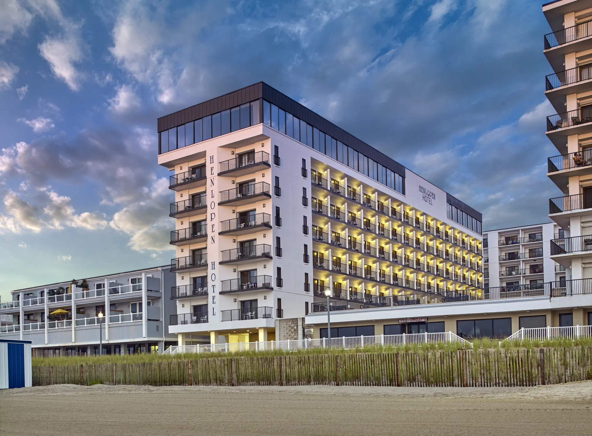 Henlopen Hotel multi-story oceanfront building with illuminated balconies at dusk beside a beach boardwalk