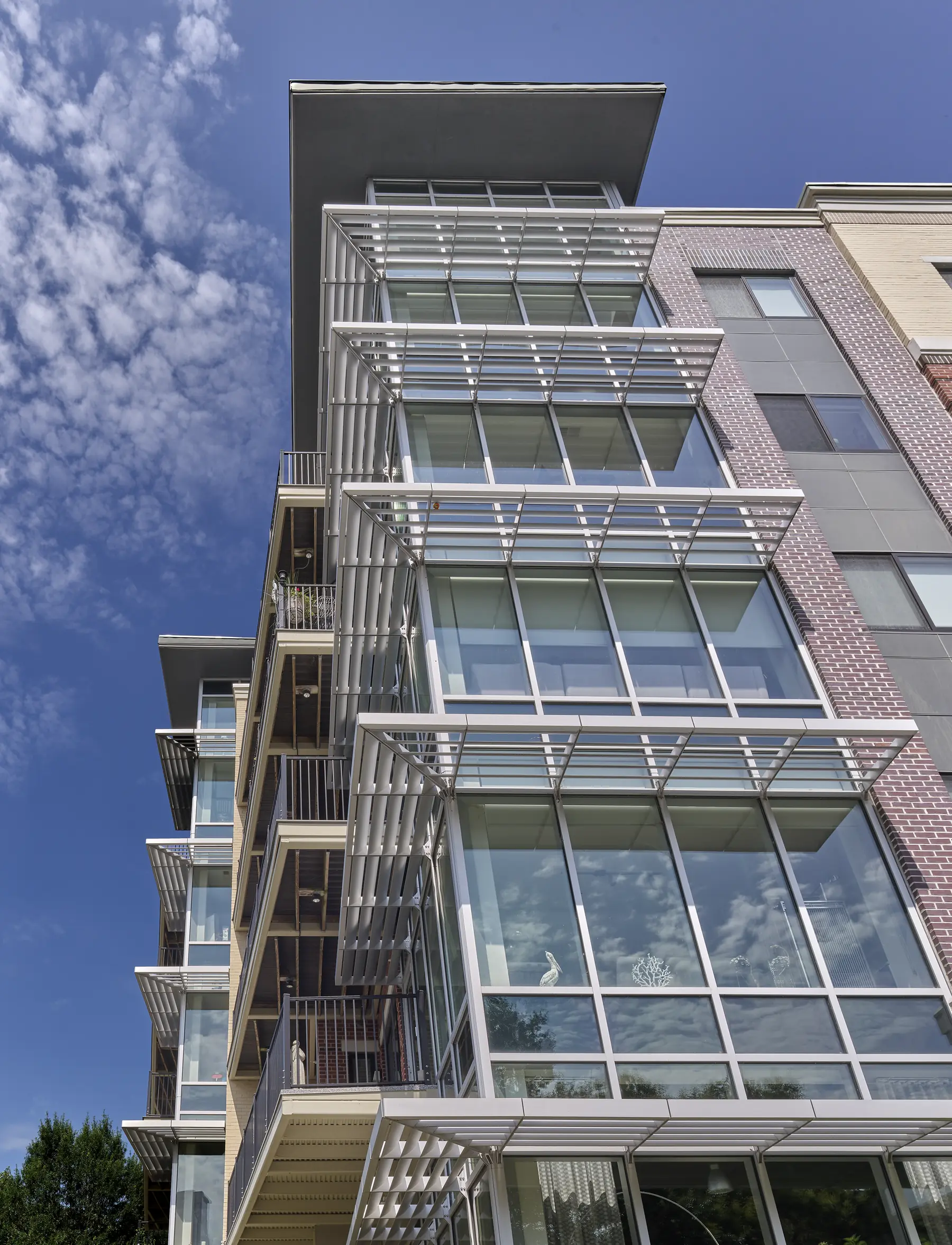 Upward view of a modern high-rise residential building with glass balconies and brick facade against a blue sky