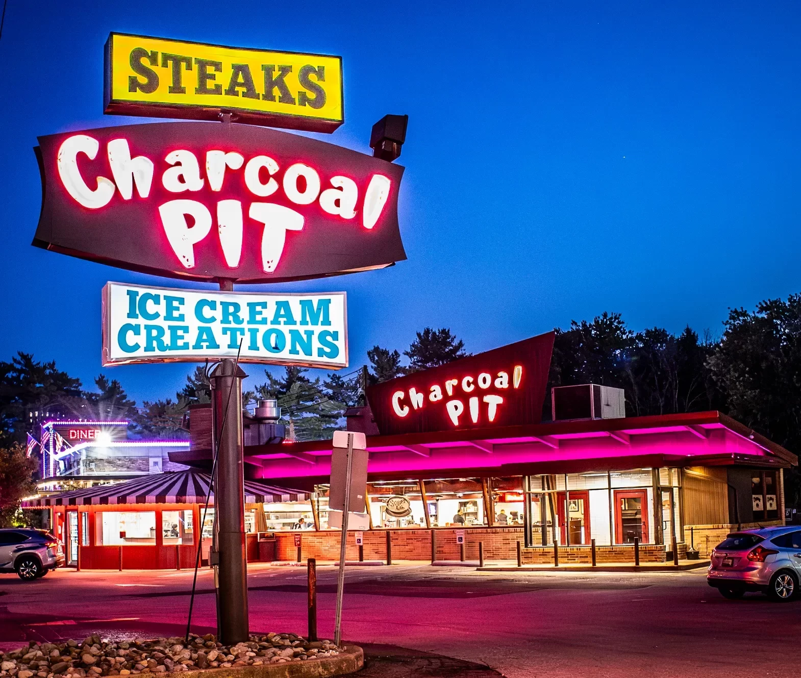 Illuminated Charcoal Pit restaurant sign advertising steaks and ice cream creations above the diner at dusk.
