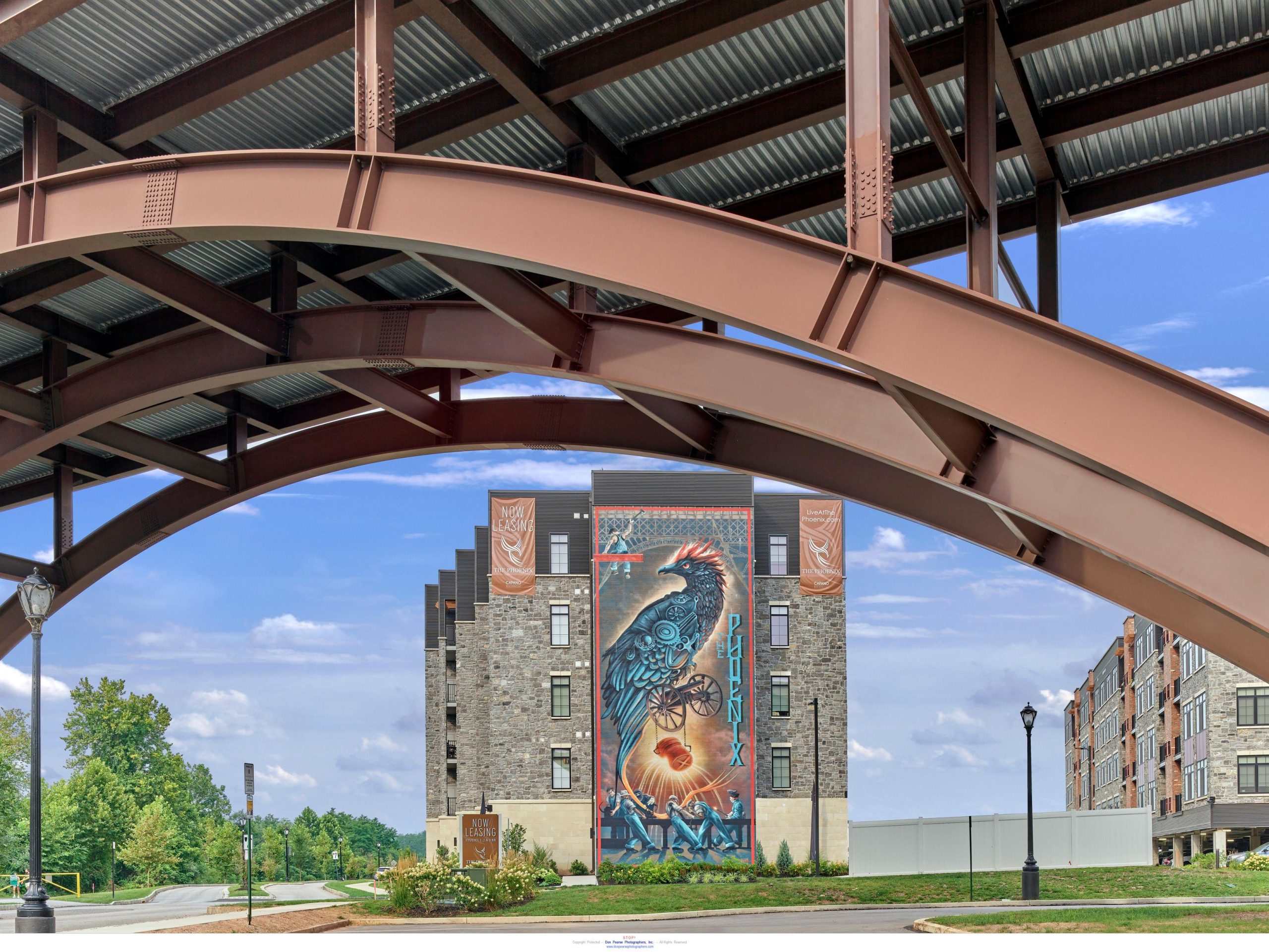 A phoenix bird mural adorns The Phoenix apartment building, viewed beneath a curved steel canopy structure in Wilmington, DE.