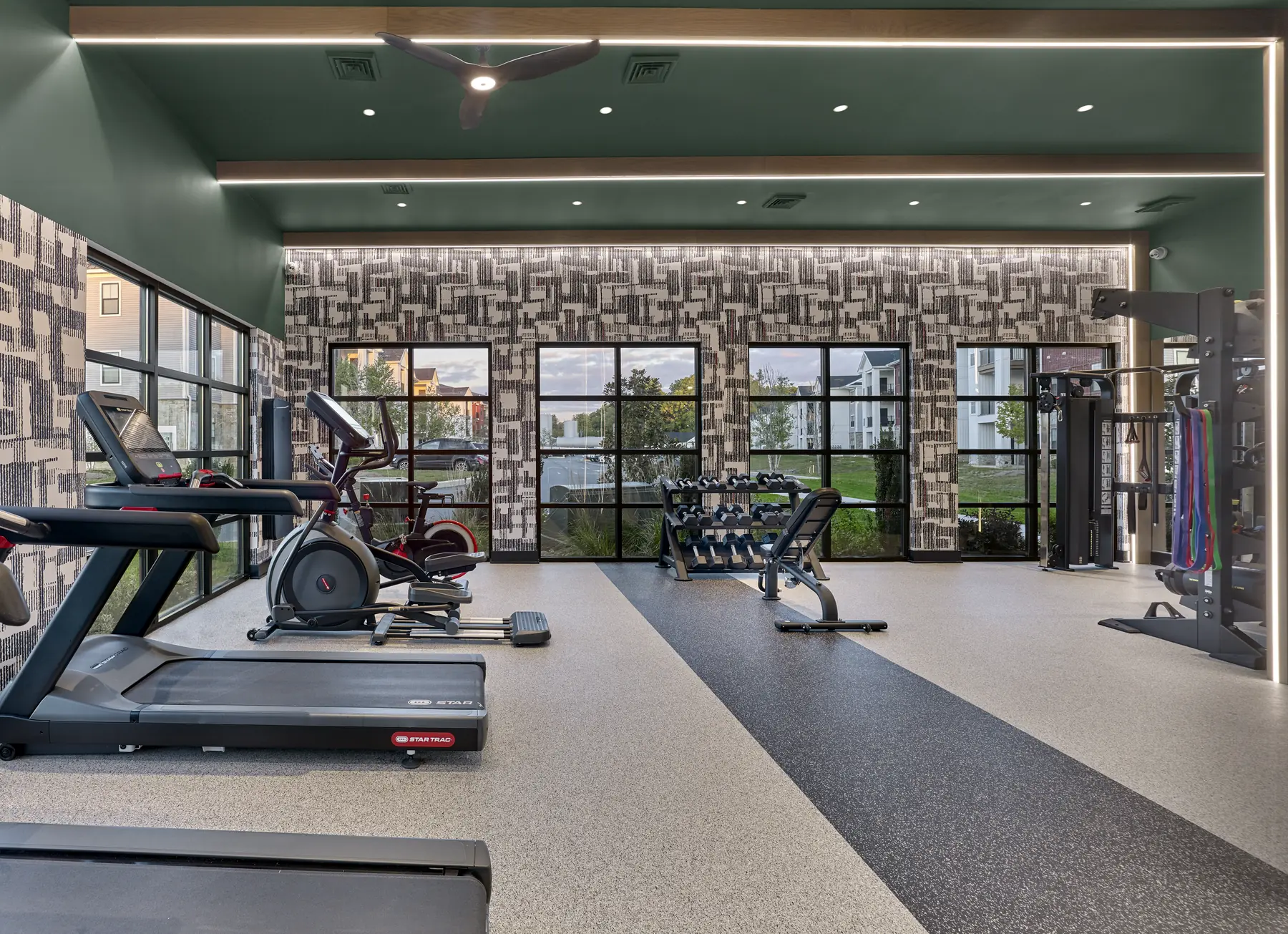 Fitness center with treadmills, elliptical machines, free weights, and a cable exercise station near large windows.