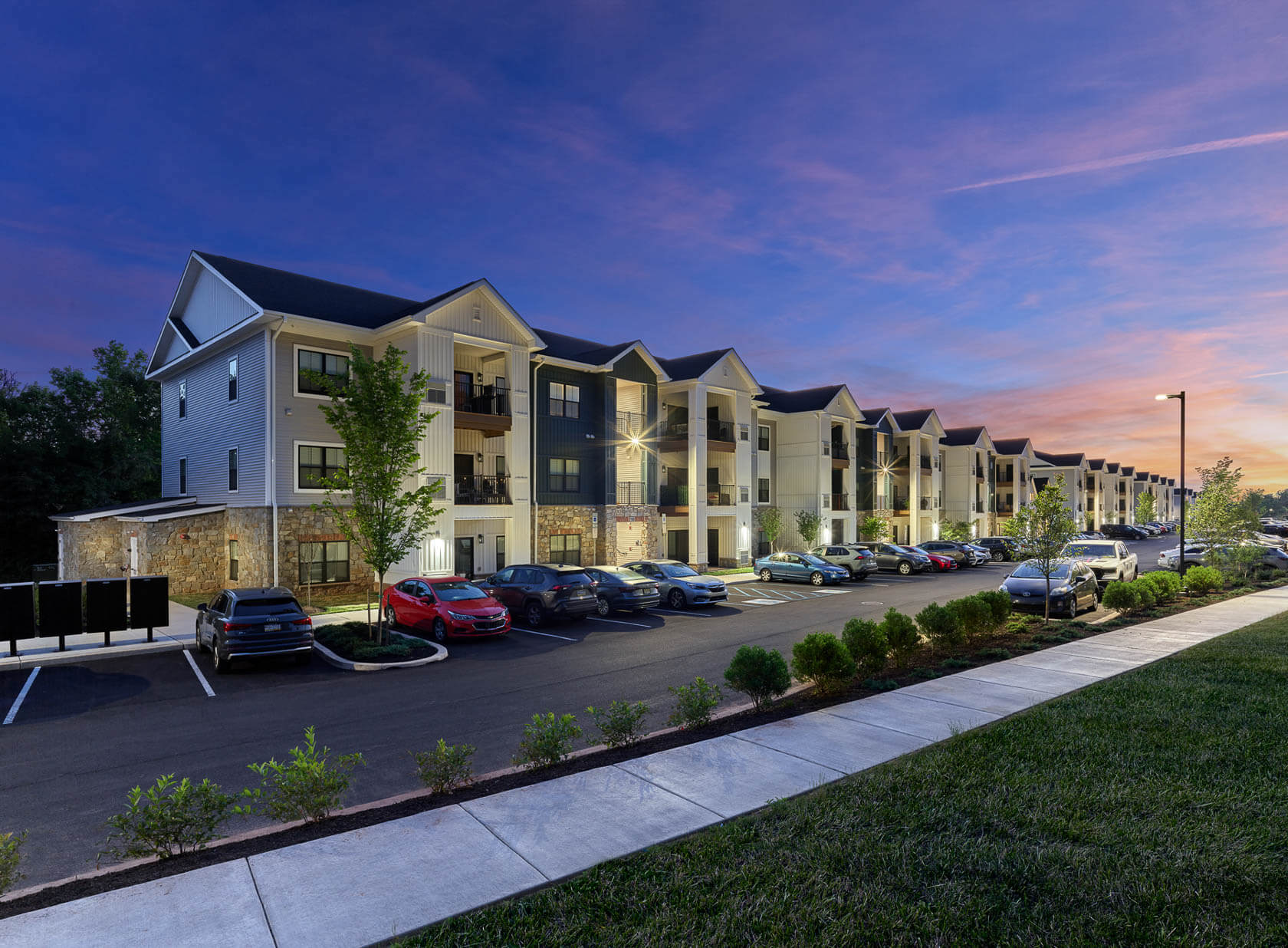 Three-story apartment building at The Reserve on Forge with parking lot and landscaped walkway at dusk