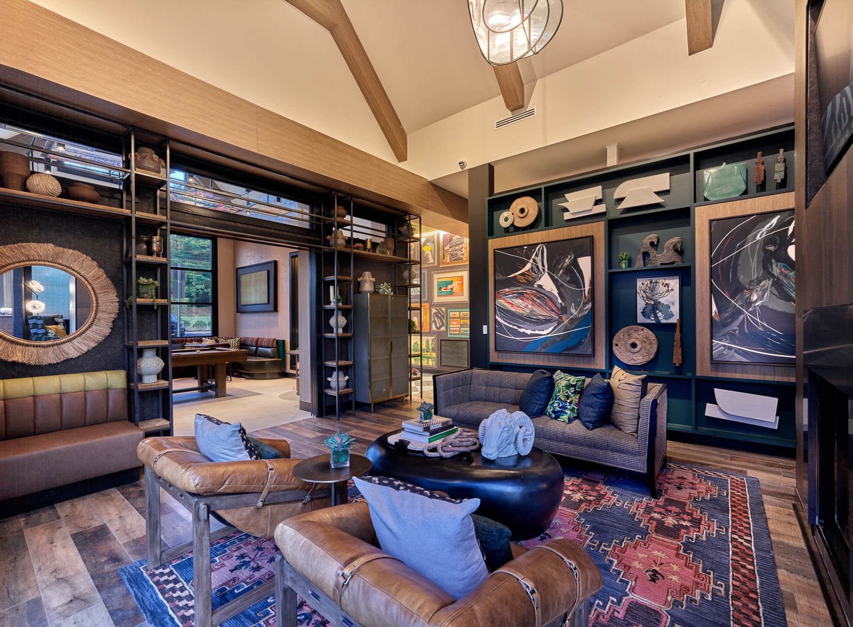 Lounge area with leather armchairs, patterned rug, artwork-filled walls, and open shelving displaying decor.
