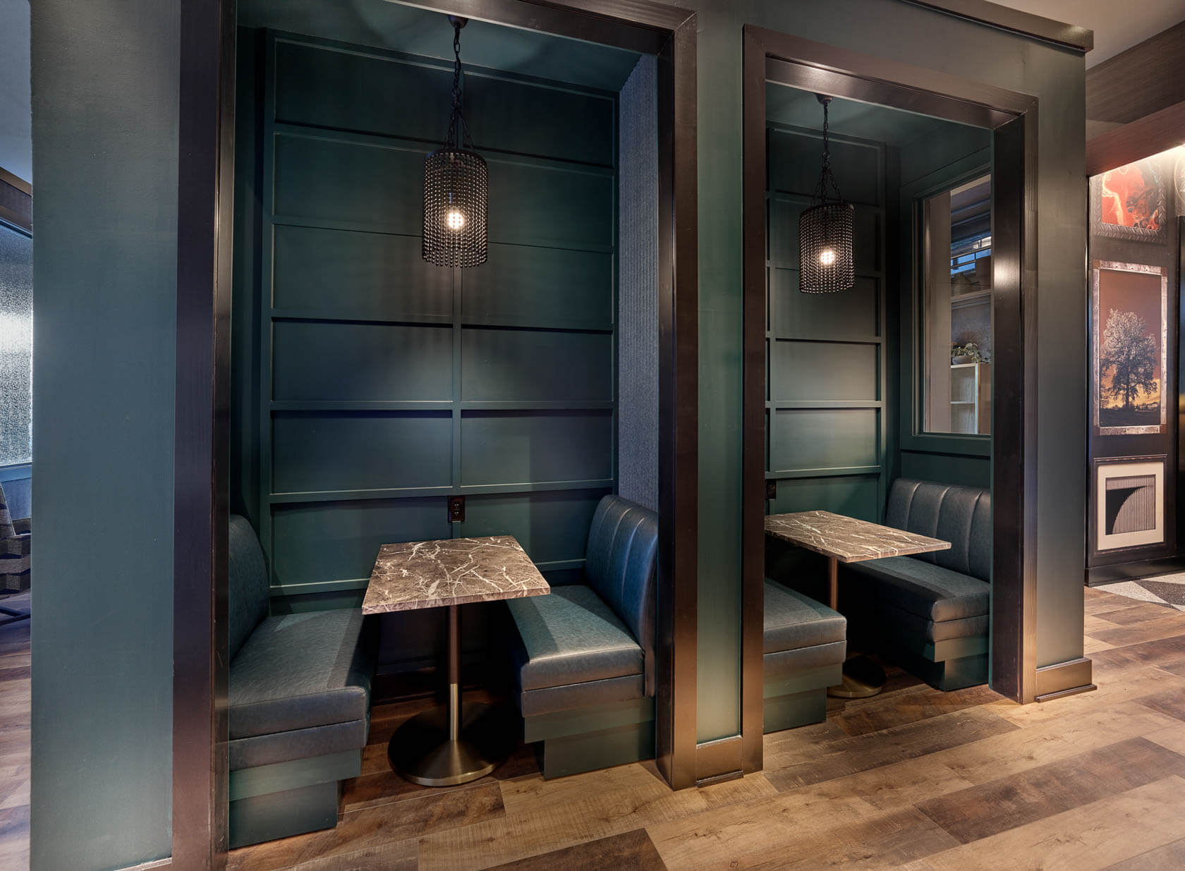 Two private booth seating nooks with dark teal paneling, marble tables, and pendant lighting in a lounge area