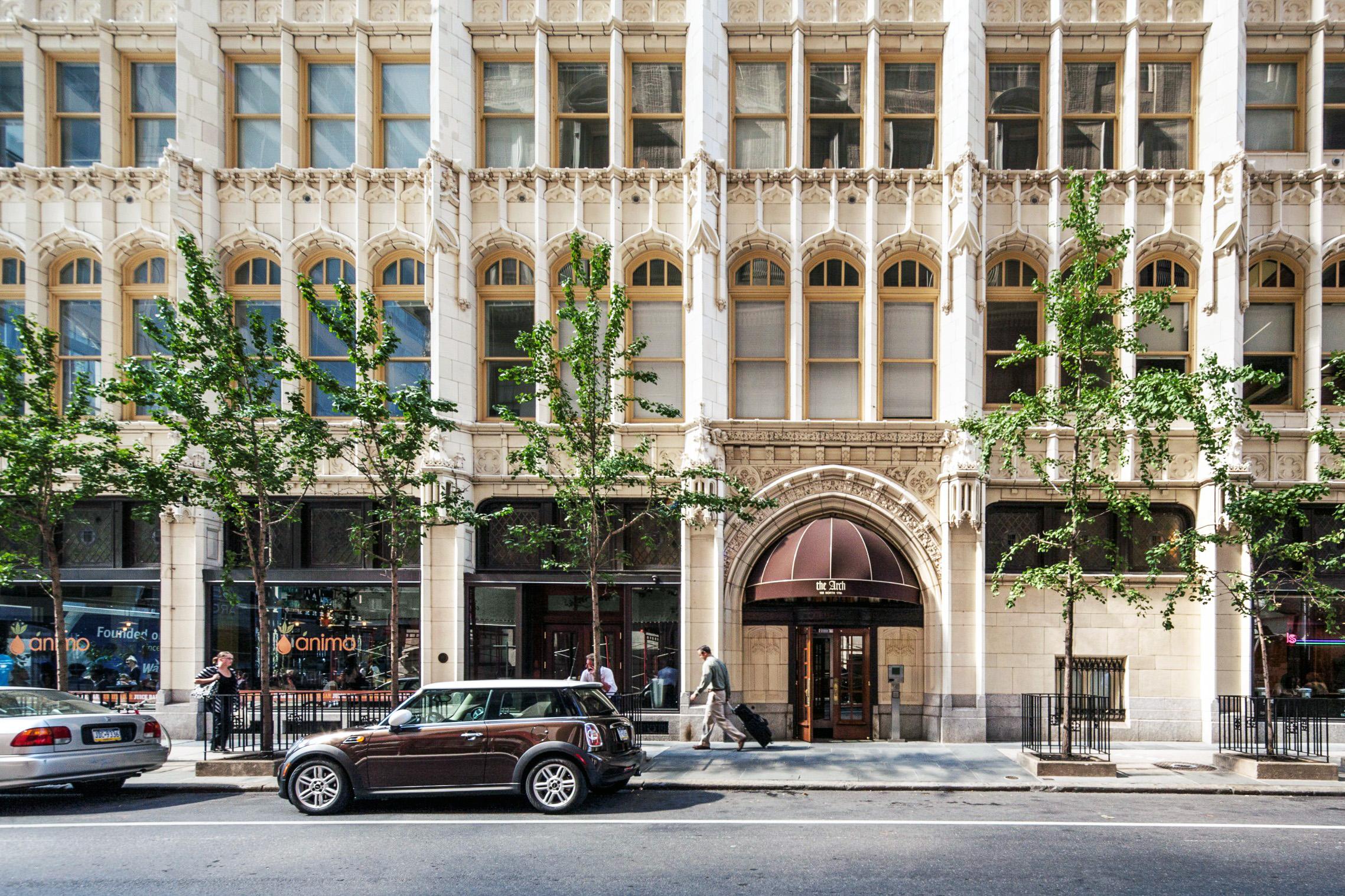 Ornate arched entrance of The Arch apartment building with a maroon awning on a tree-lined city street