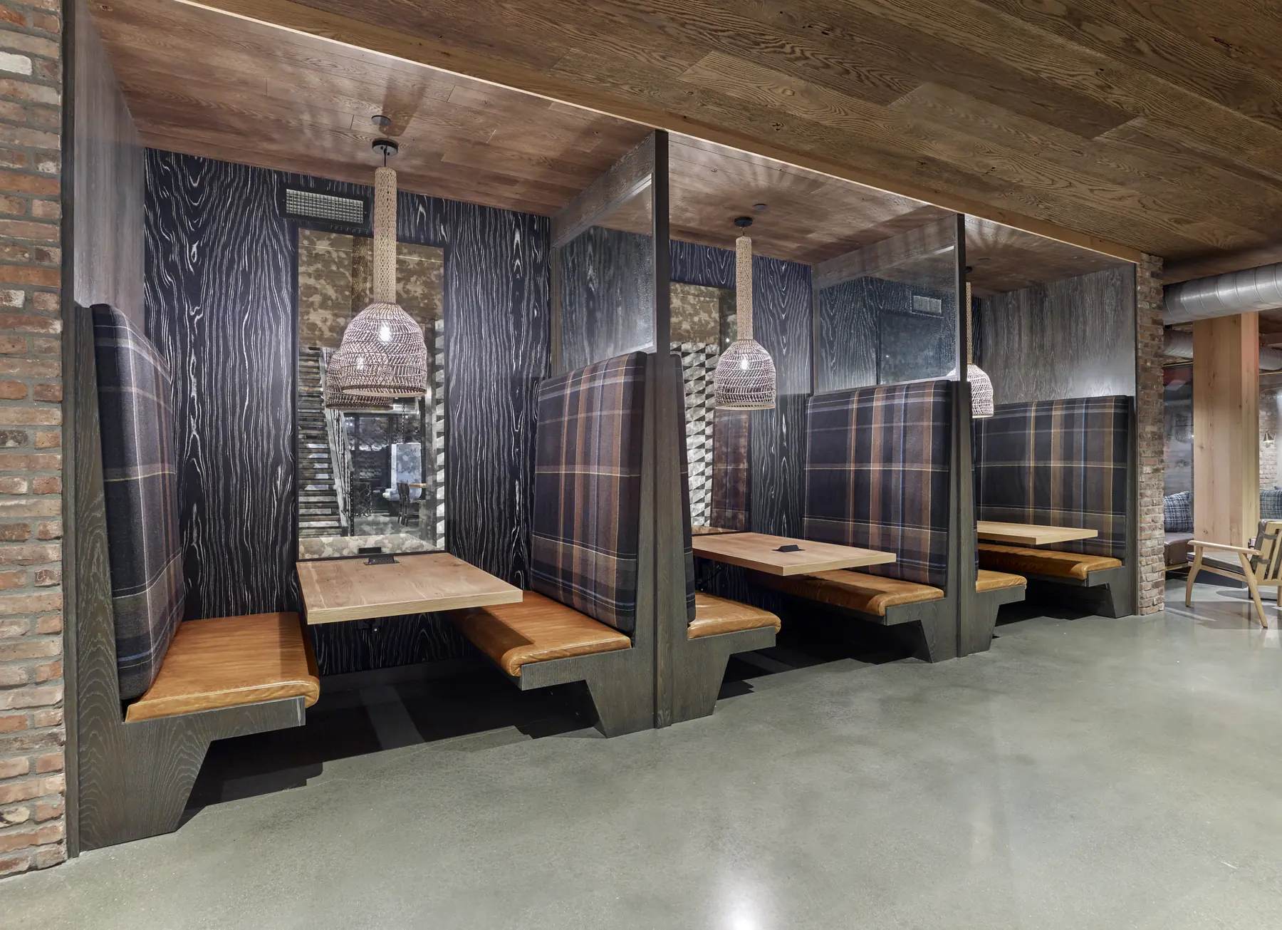 Booth seating with plaid upholstery, wood-grain paneling, and pendant lighting in a restaurant dining area