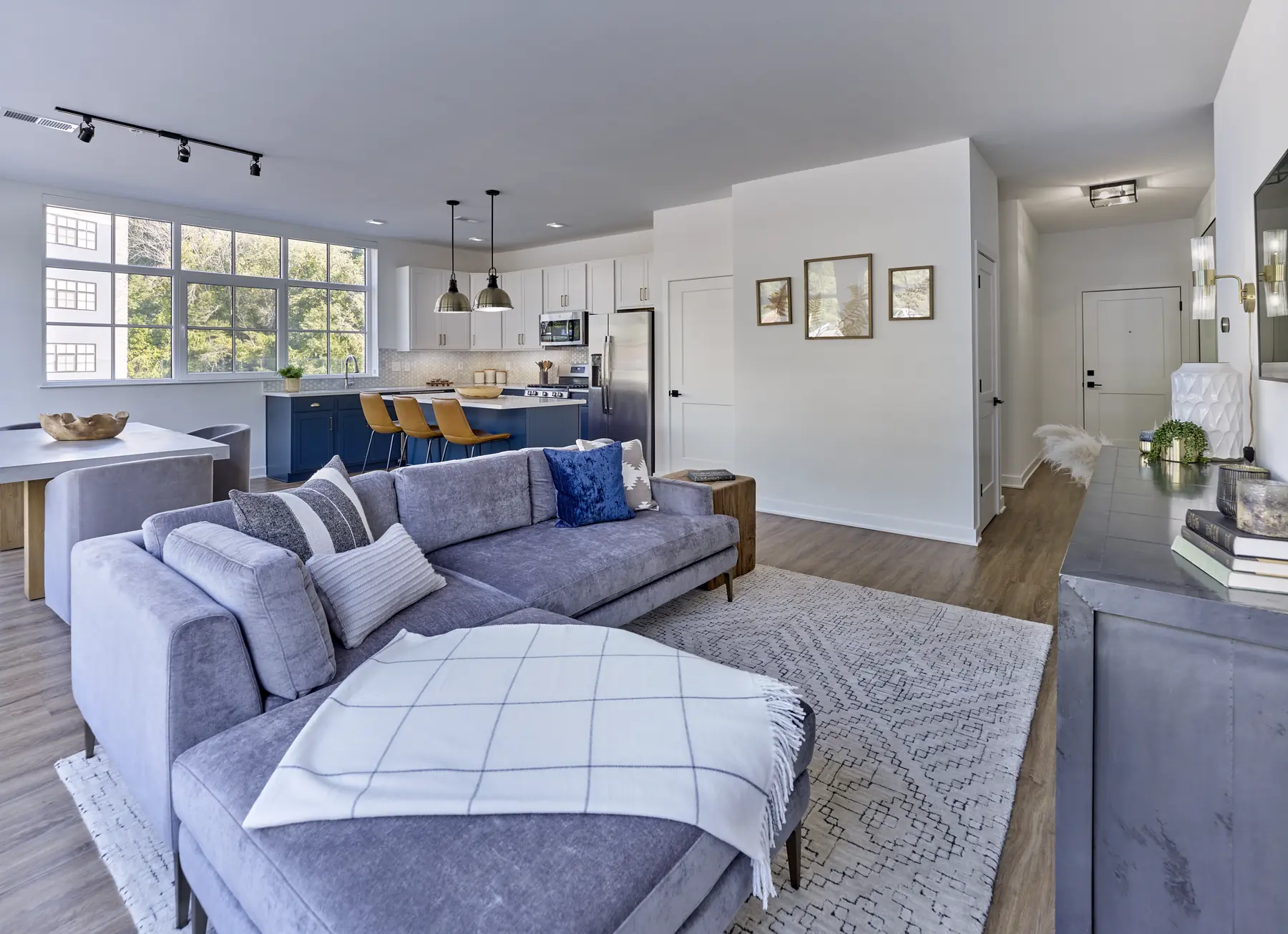 Open-concept living room with gray sectional sofa, area rug, and view into kitchen with blue cabinetry