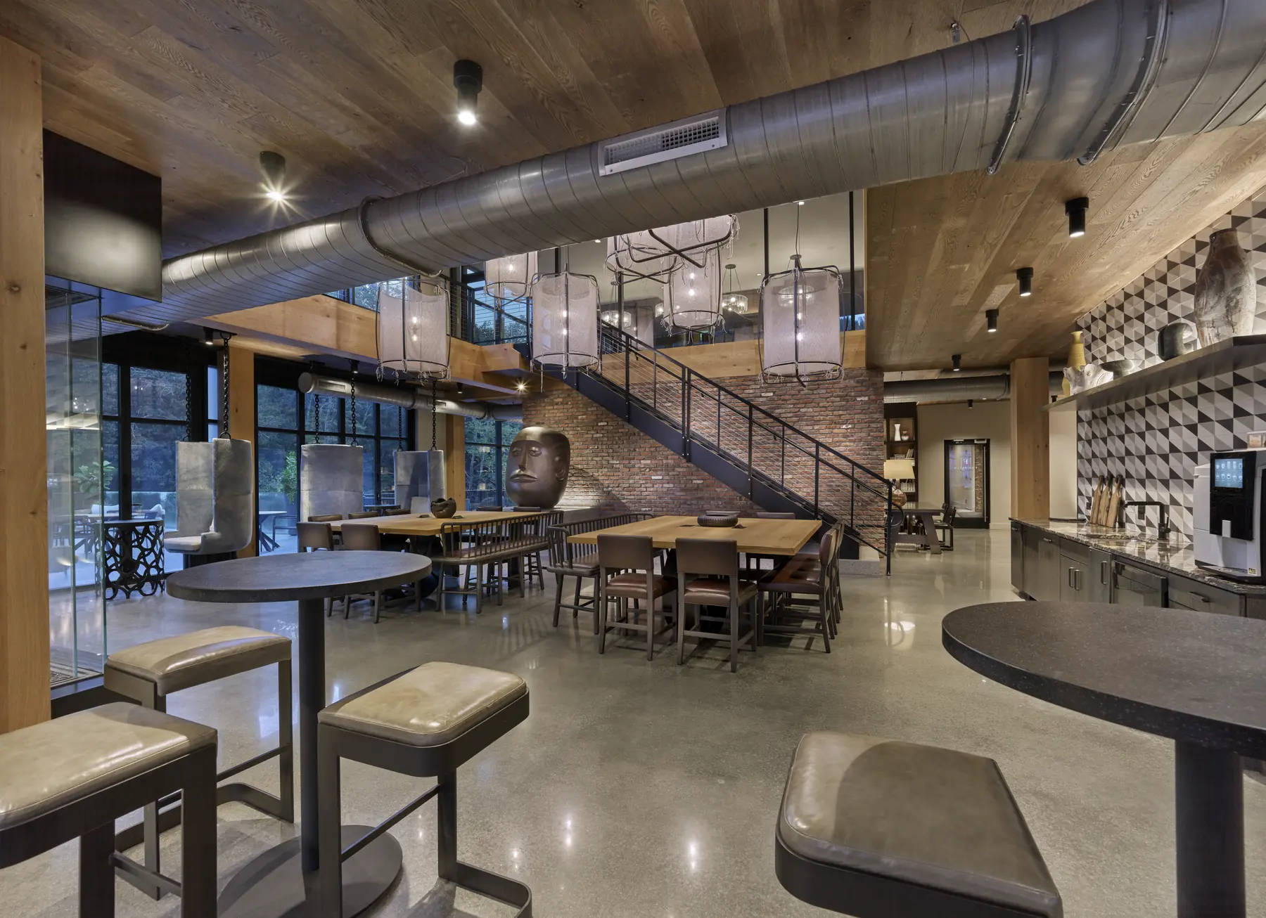 Industrial-style lounge with exposed ductwork, wooden ceiling, staircase, and communal seating areas at The Falls