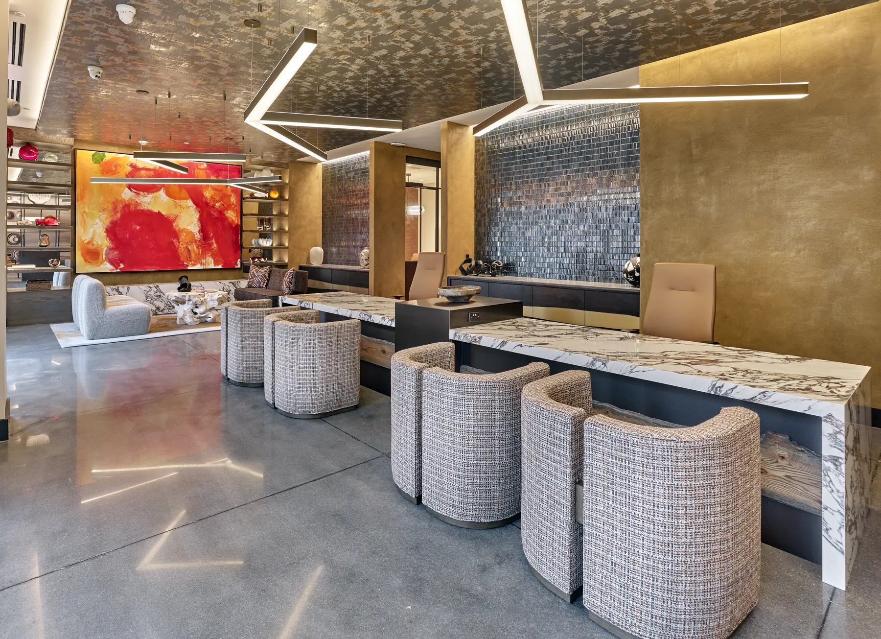 Modern lobby seating area with marble reception counter, tweed barrel chairs, and a bold red abstract painting.