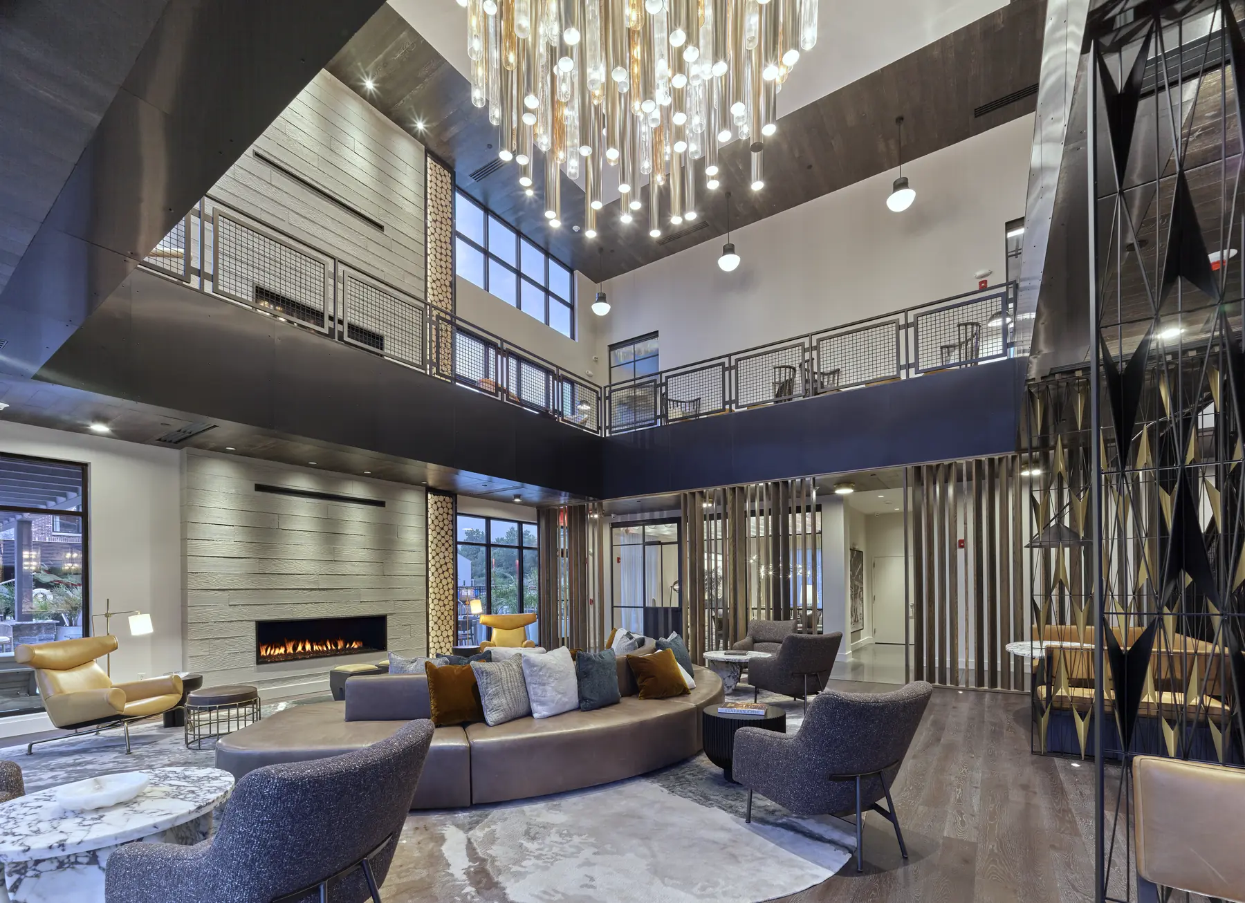 Two-story lounge with sculptural glass chandelier, fireplace, plush seating and open loft balcony above