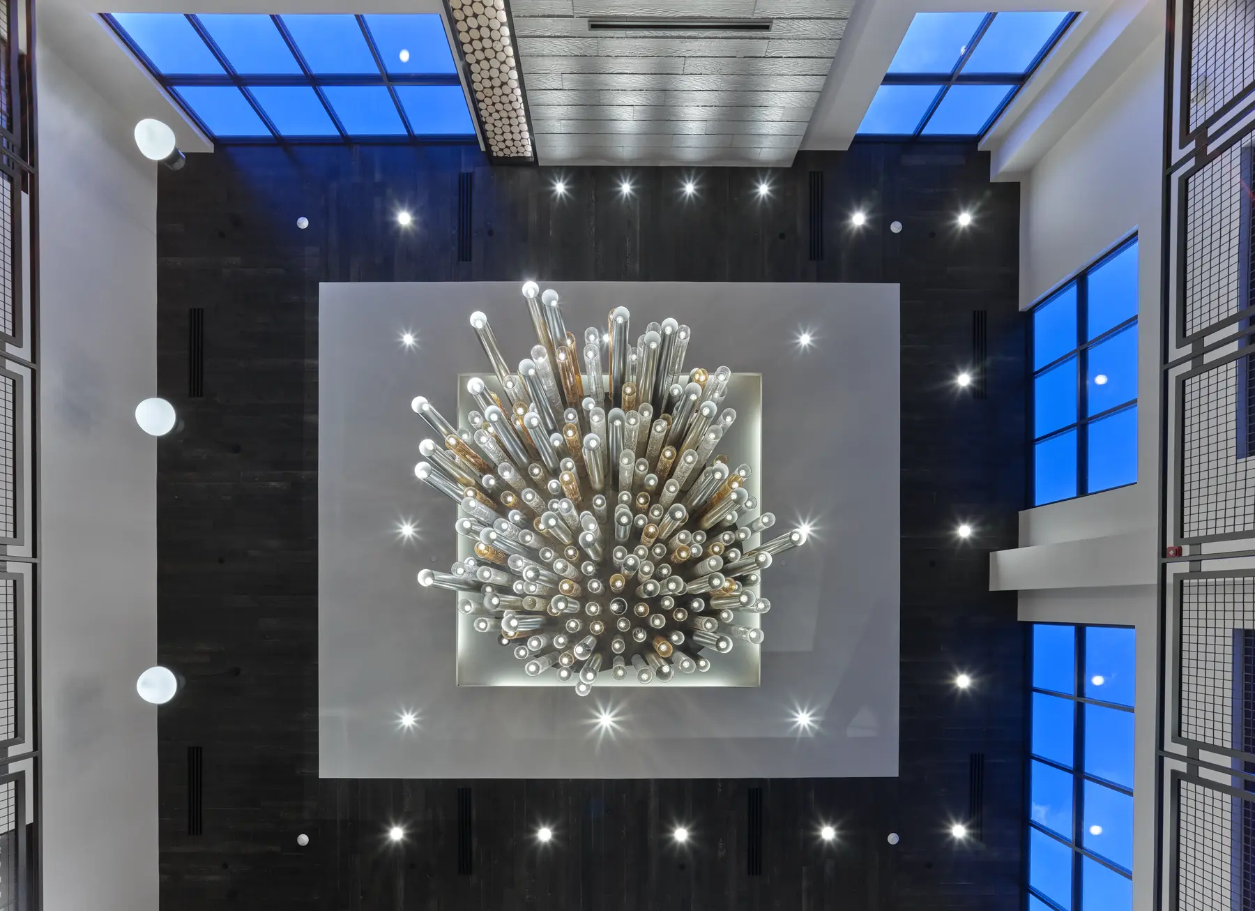 Aerial view of a lobby atrium featuring a starburst sculpture chandelier surrounded by dark wood walls and skylights