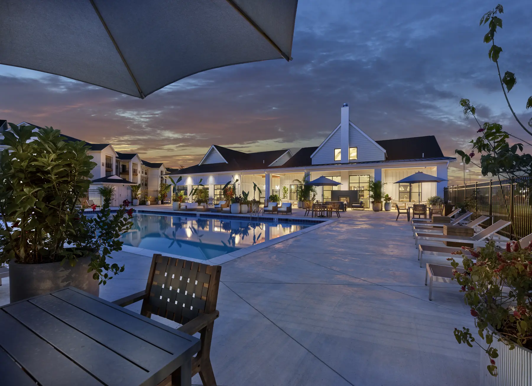 Twilight view of a resort-style pool with lounge chairs, umbrellas, and a lit clubhouse at The Reserve at Westown