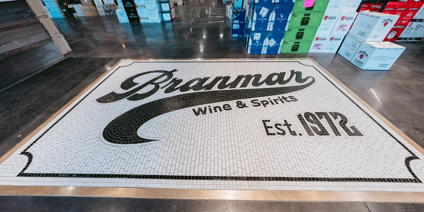 Mosaic tile floor with the Branmar Wine & Spirits logo and Est. 1972 date at store entrance, surrounded by stacked liquor cases.