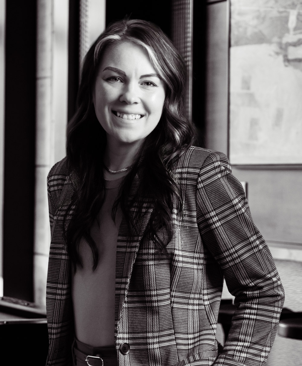 Smiling woman with long wavy hair wears a plaid blazer in a black and white portrait