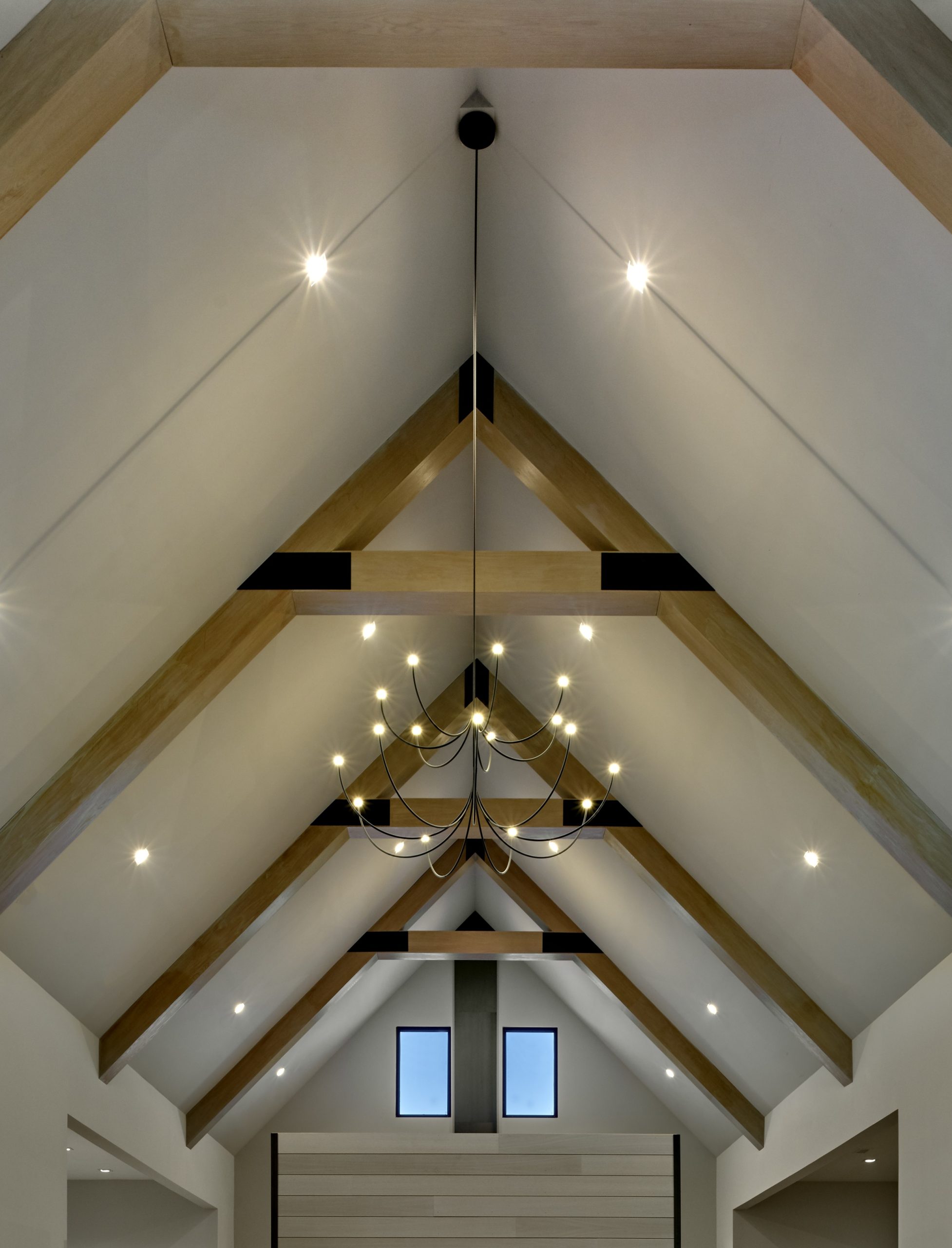 Vaulted wood-beamed ceiling with a modern chandelier and recessed lighting above a peaked hallway