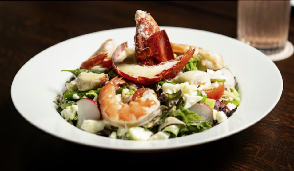 Seafood salad with lobster claw, shrimp, radishes, tomatoes, and mixed greens on a white plate
